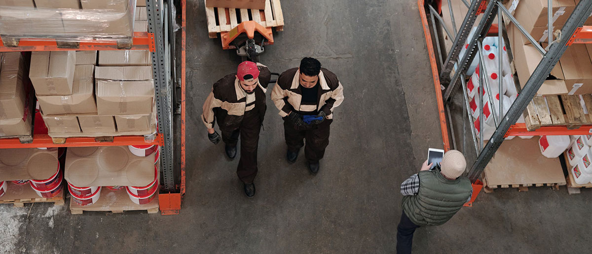 Tres hombres  trabajando en almacén con tablet y carretilla de palets
