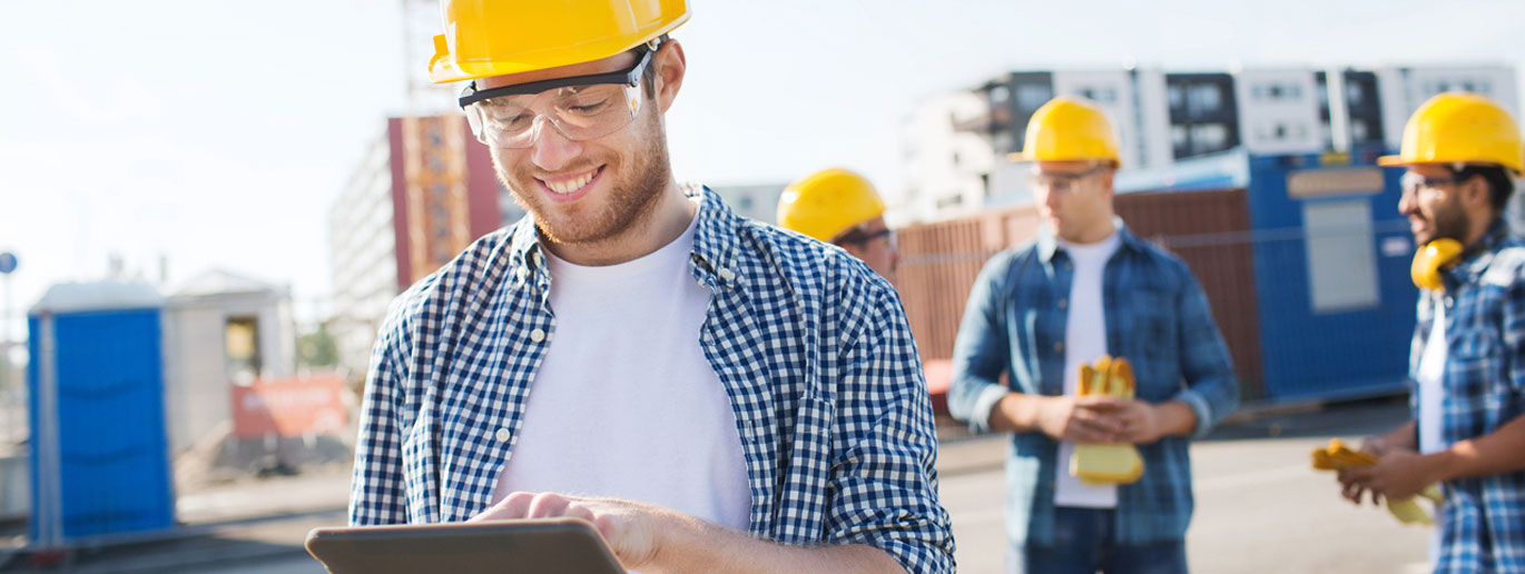 Trabajo remoto de jefe de obra consultando planos en una tablet con su equipo de peones de construcción