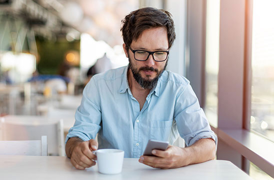 Hombre tomando café viendo el móvil en una cafetería