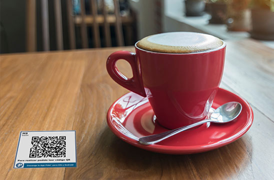 Taza de café y pegatina con código QR en la mesa de una cafetería