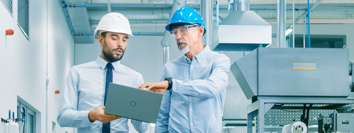 Dos supervisores con casco en una fábrica viendo proyecto en un portátil